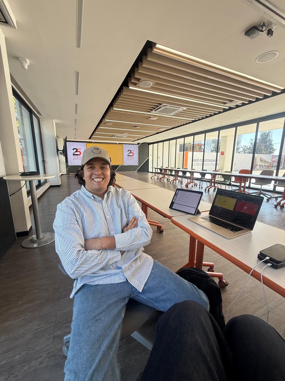 Andrés sonriendo, sentado junto a una mesa con su computadora.